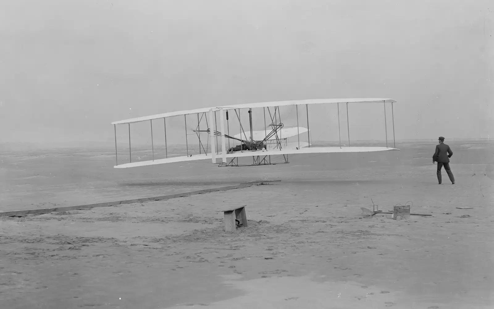 Orville takes to the air in the flyer for the first time as Wilbur assists.
