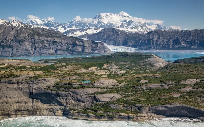 Glaciers loom over the ocean with large snowy mountains rising into blue skies